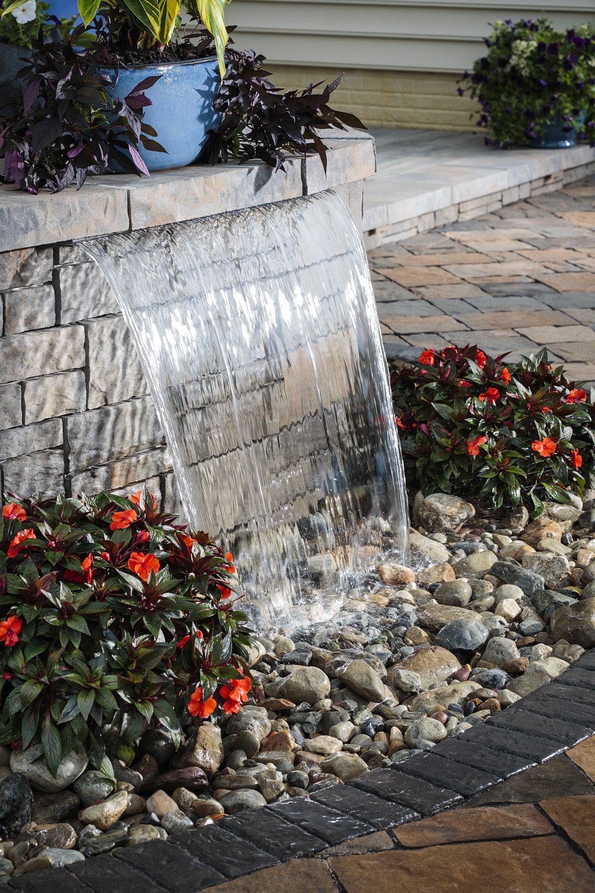 Sheer water fountain spilling from a stone wall into river rock