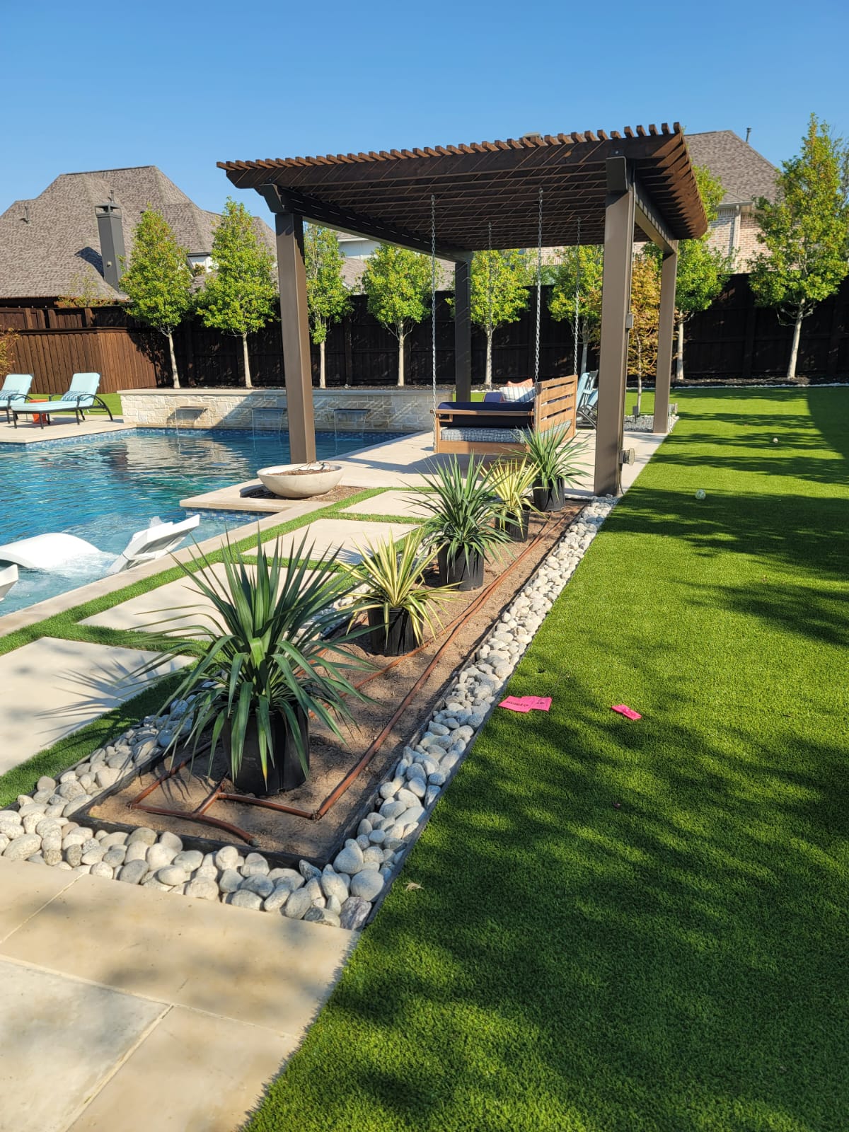 Backyard pool with pergola, artificial turf and river-rock planting bed